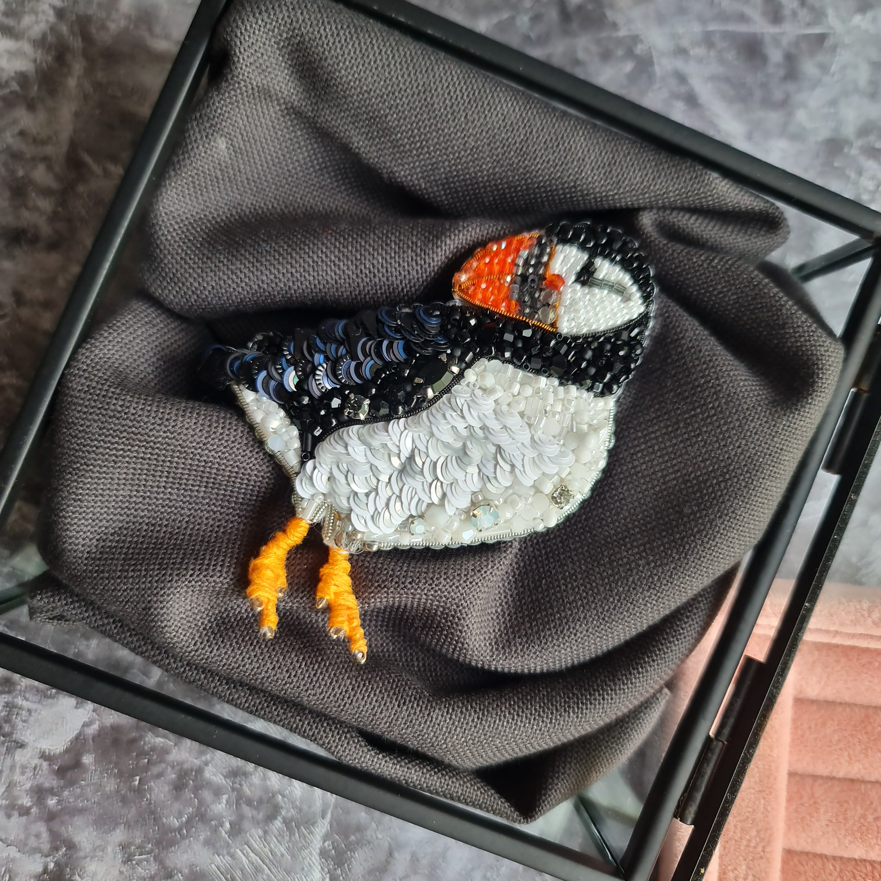 Sequined puffin brooch on a gray fabric background