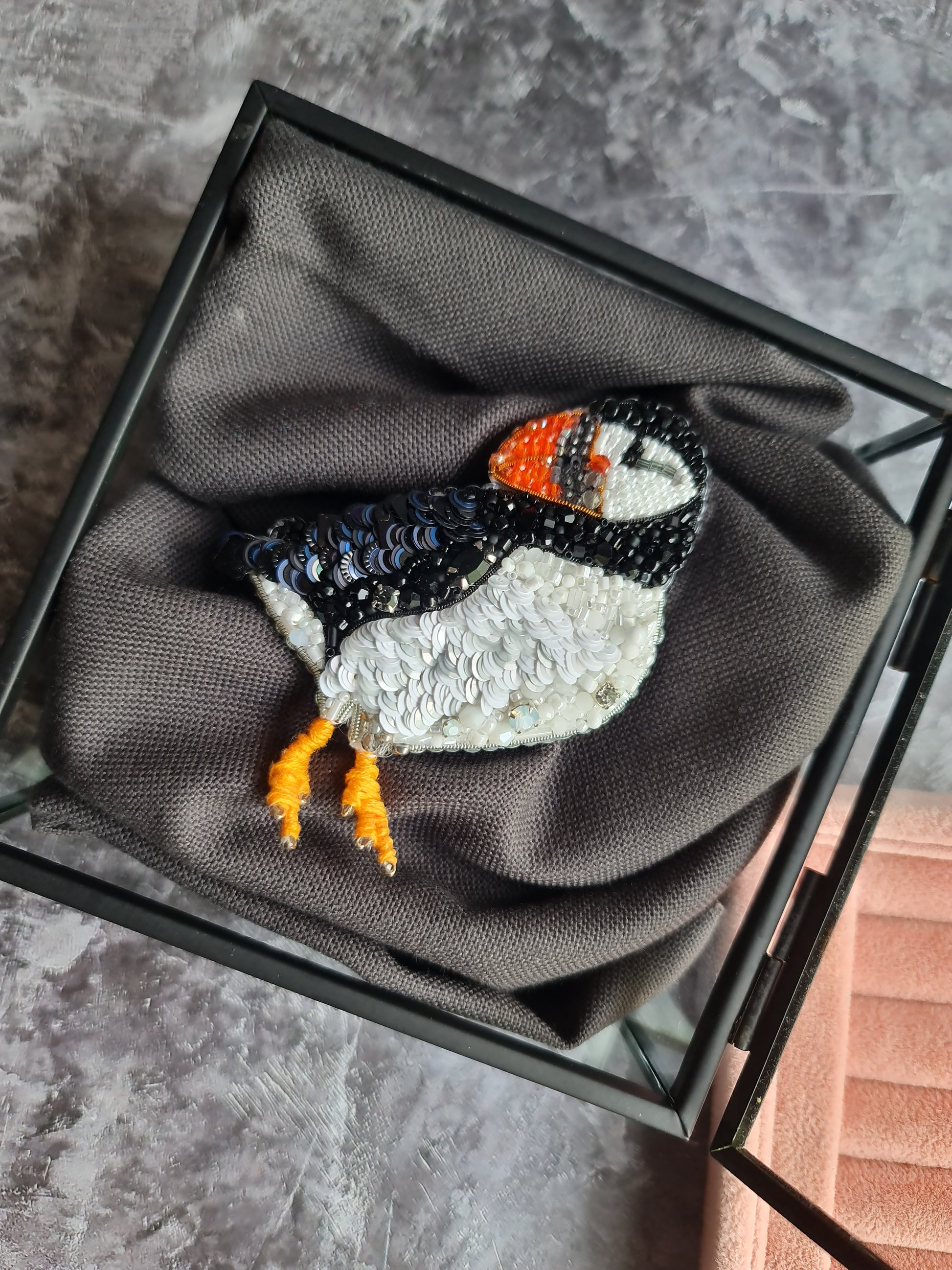 Sequined puffin brooch on a gray fabric background