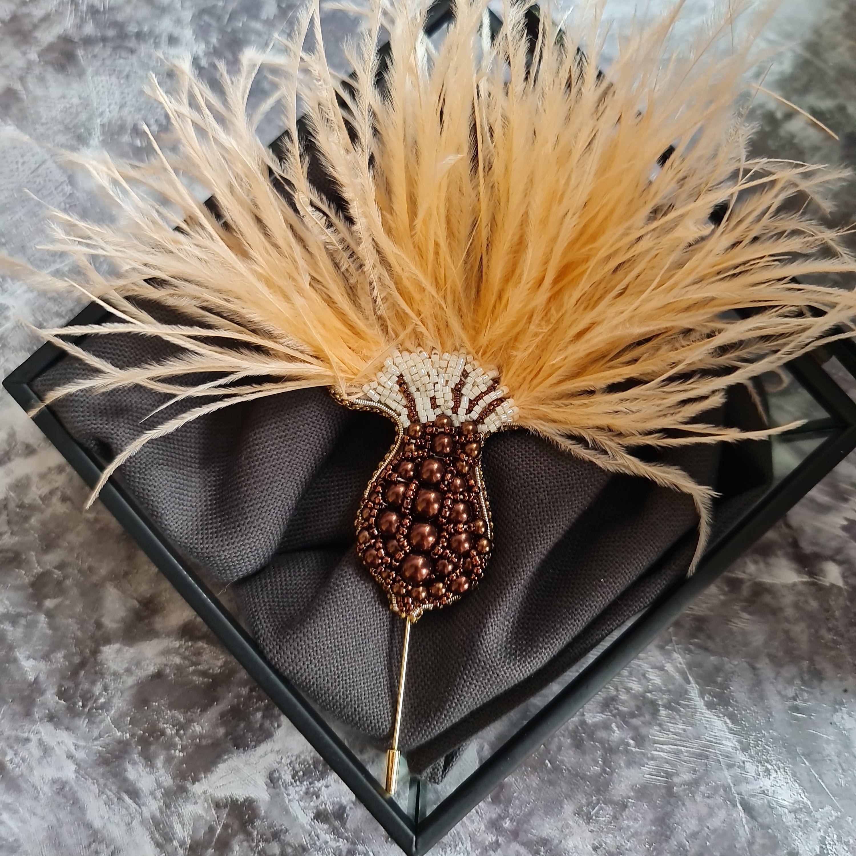 Decorative hair stick with feather and bead details in a black box on a gray marble surface