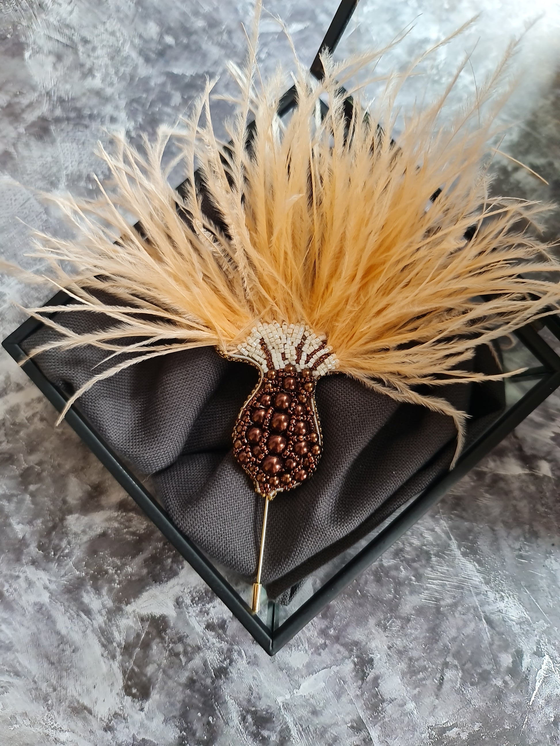 Decorative hair stick with feather and bead details in a black box on a gray marble surface