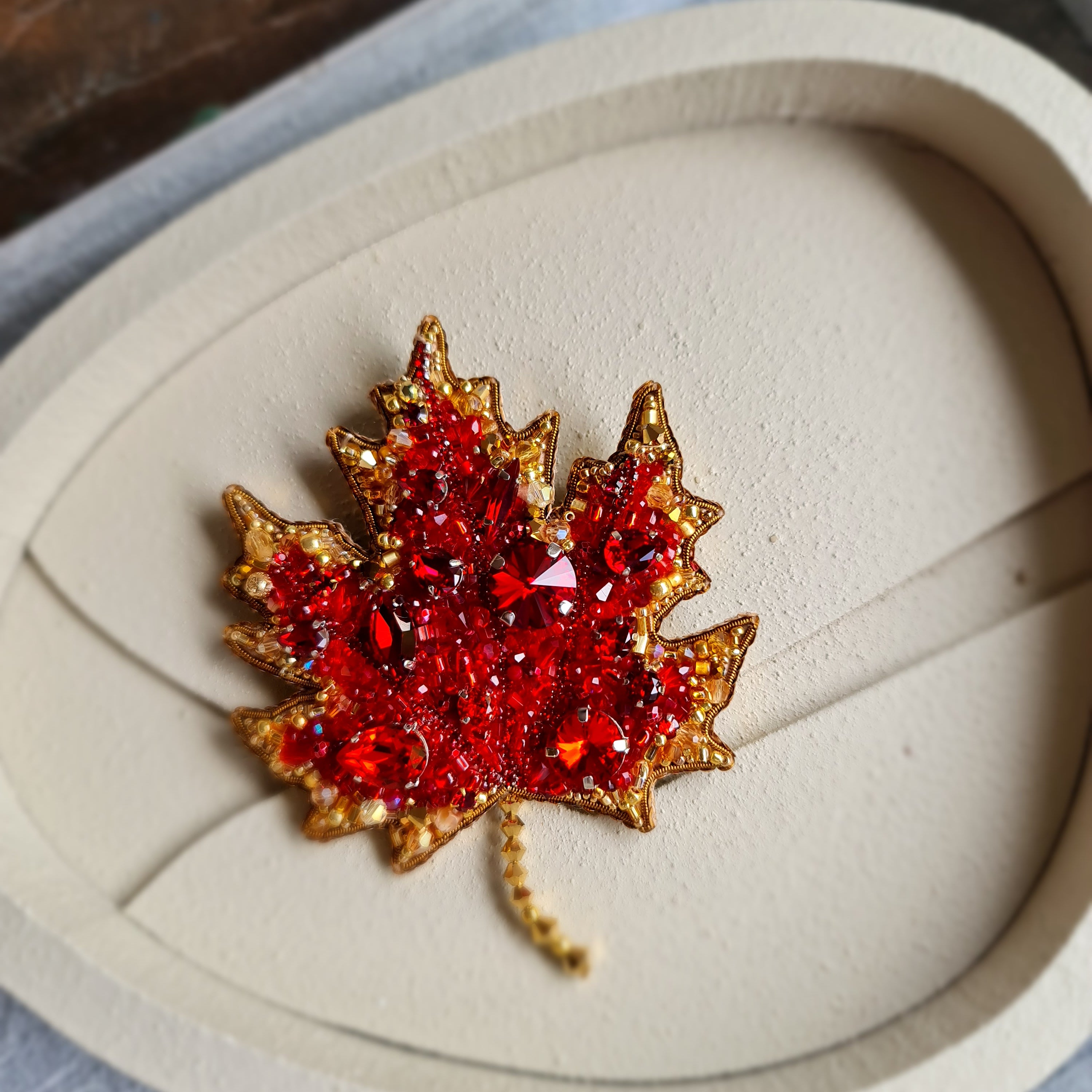 Maple leaf brooch with red gemstones on a heart-shaped display box