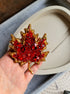 Hand holding a red gemstone brooch with gold leaves against a neutral background
