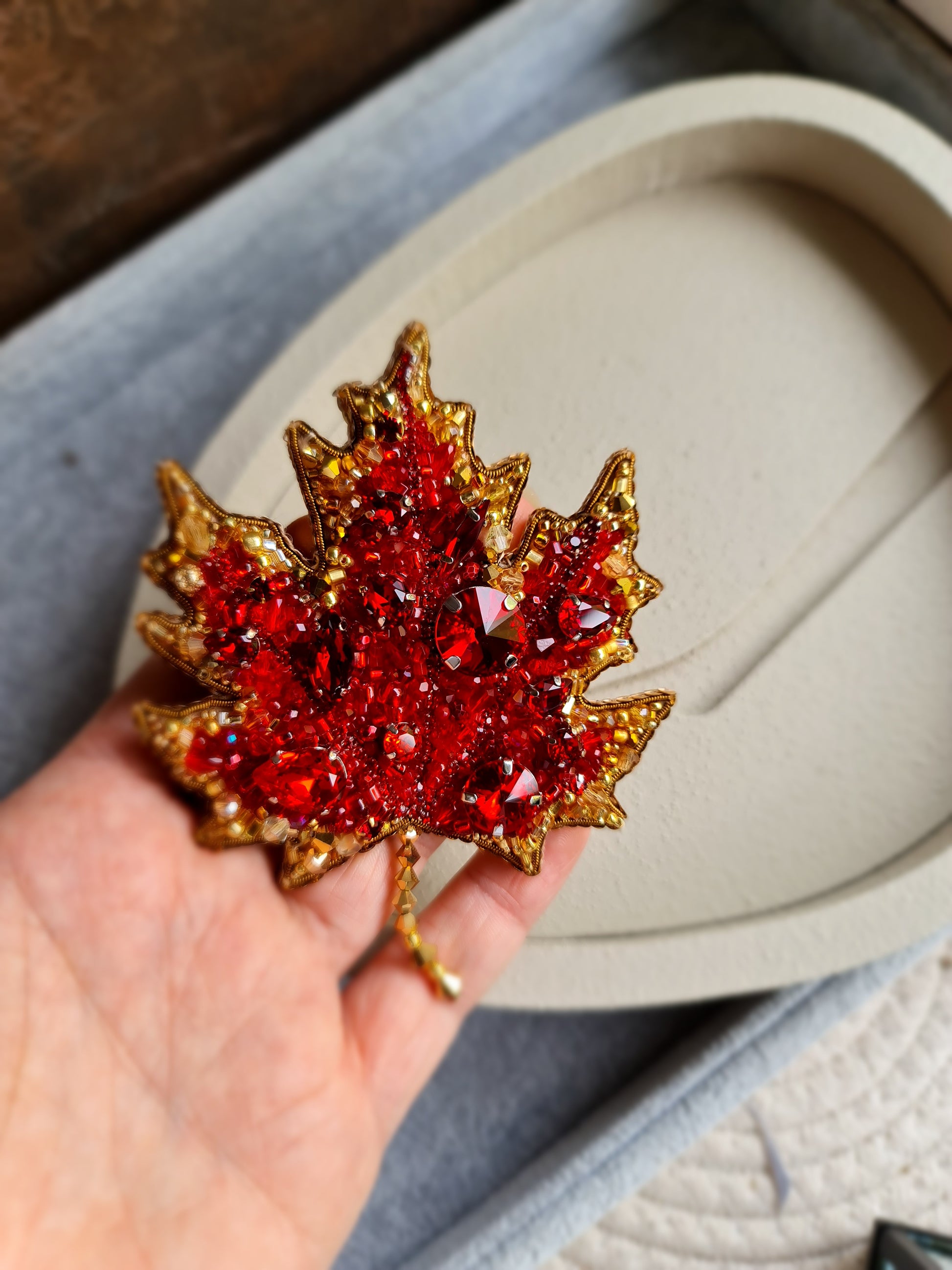 Hand holding a red gemstone brooch with gold leaves against a neutral background