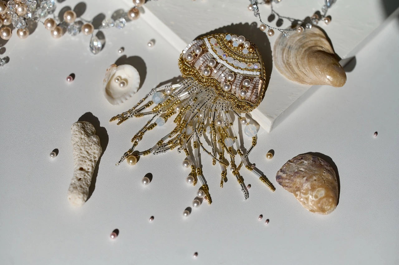 Decorative jellyfish ornament with gold accents on a white surface with shells and pearls.