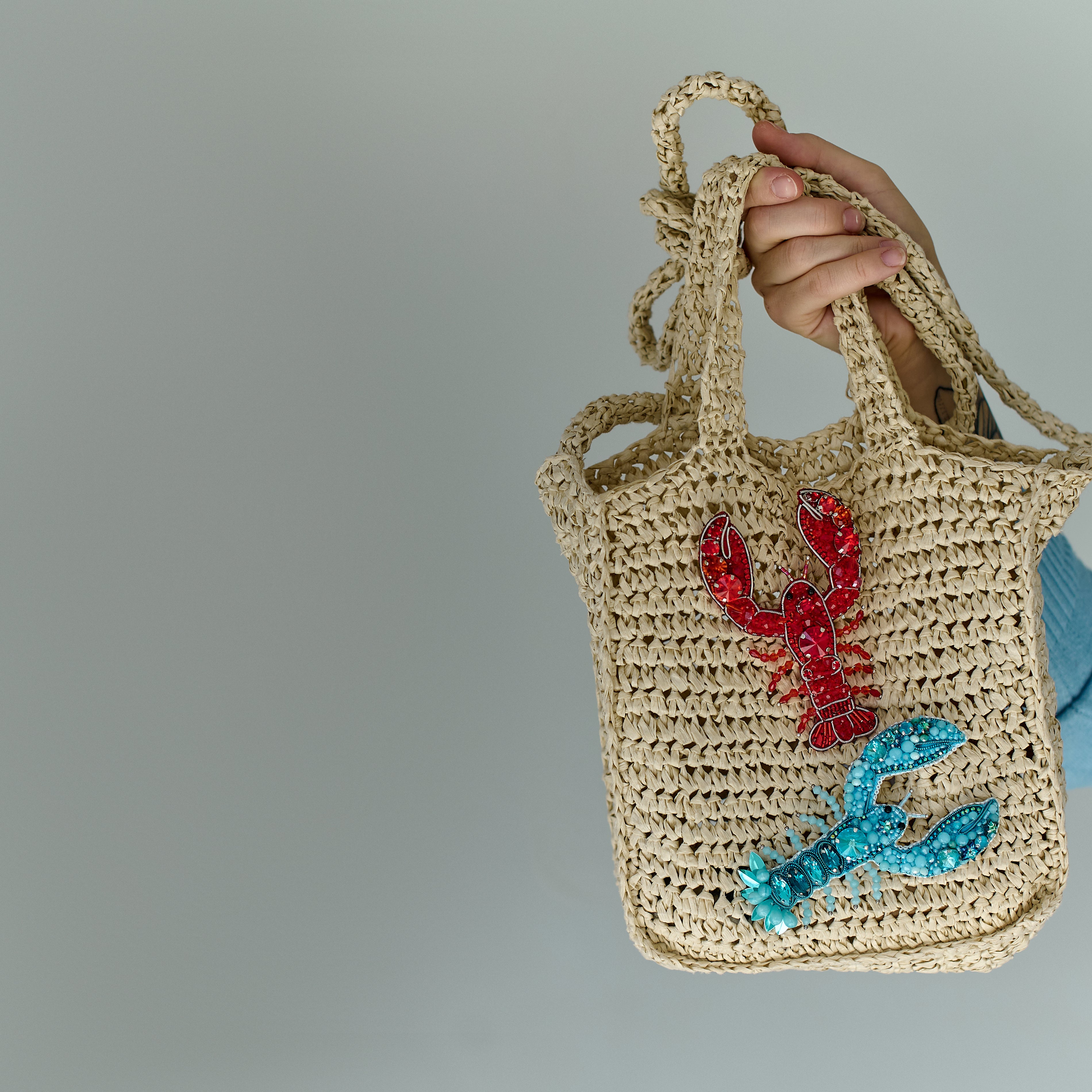 Close-up view of the intricate beadwork and secure fastening on a handmade lobster brooch, highlighting its vibrant red/blue color and ocean-inspired design