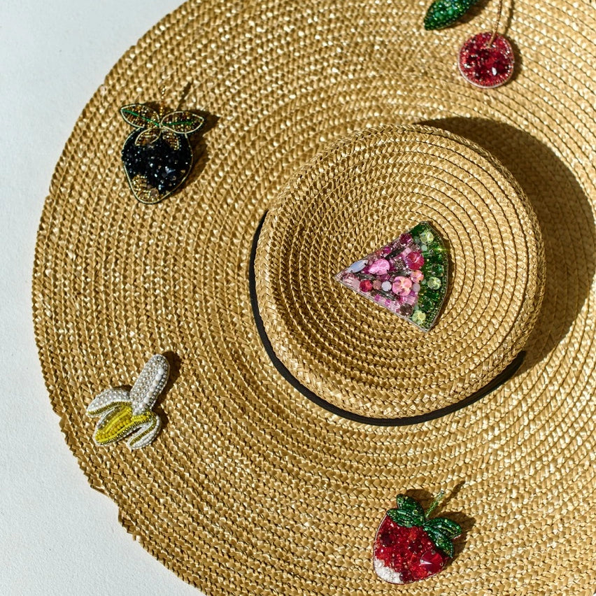 Woven straw hat with decorative fruit and pizza embellishments on a light gray background