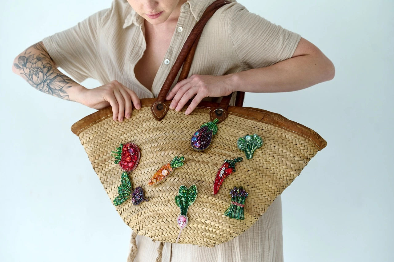 Person holding a straw bag with embroidered vegetable patterns on a light background