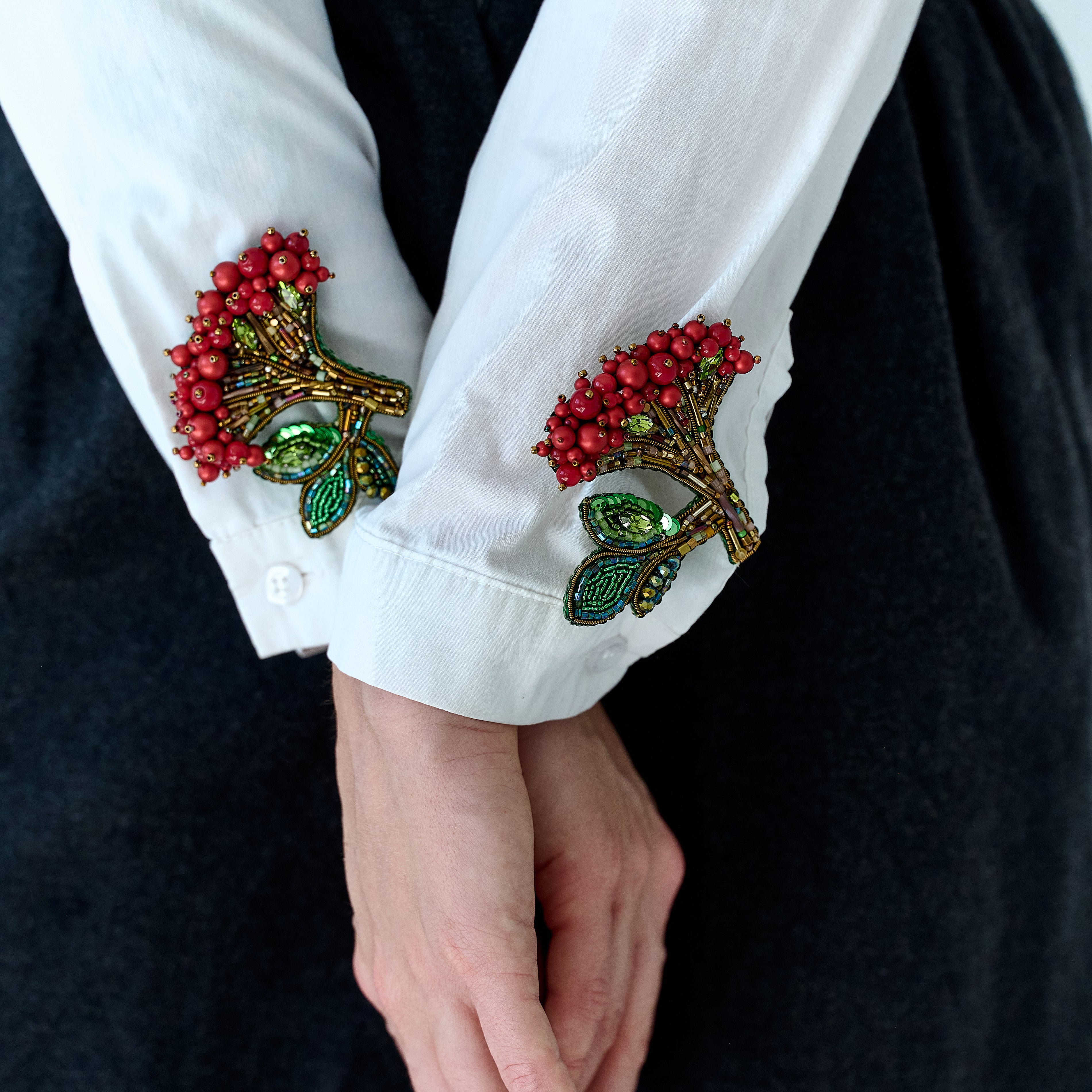 Close-up of a white shirt with decorative cuffs featuring red berries and green leaves on a black background.