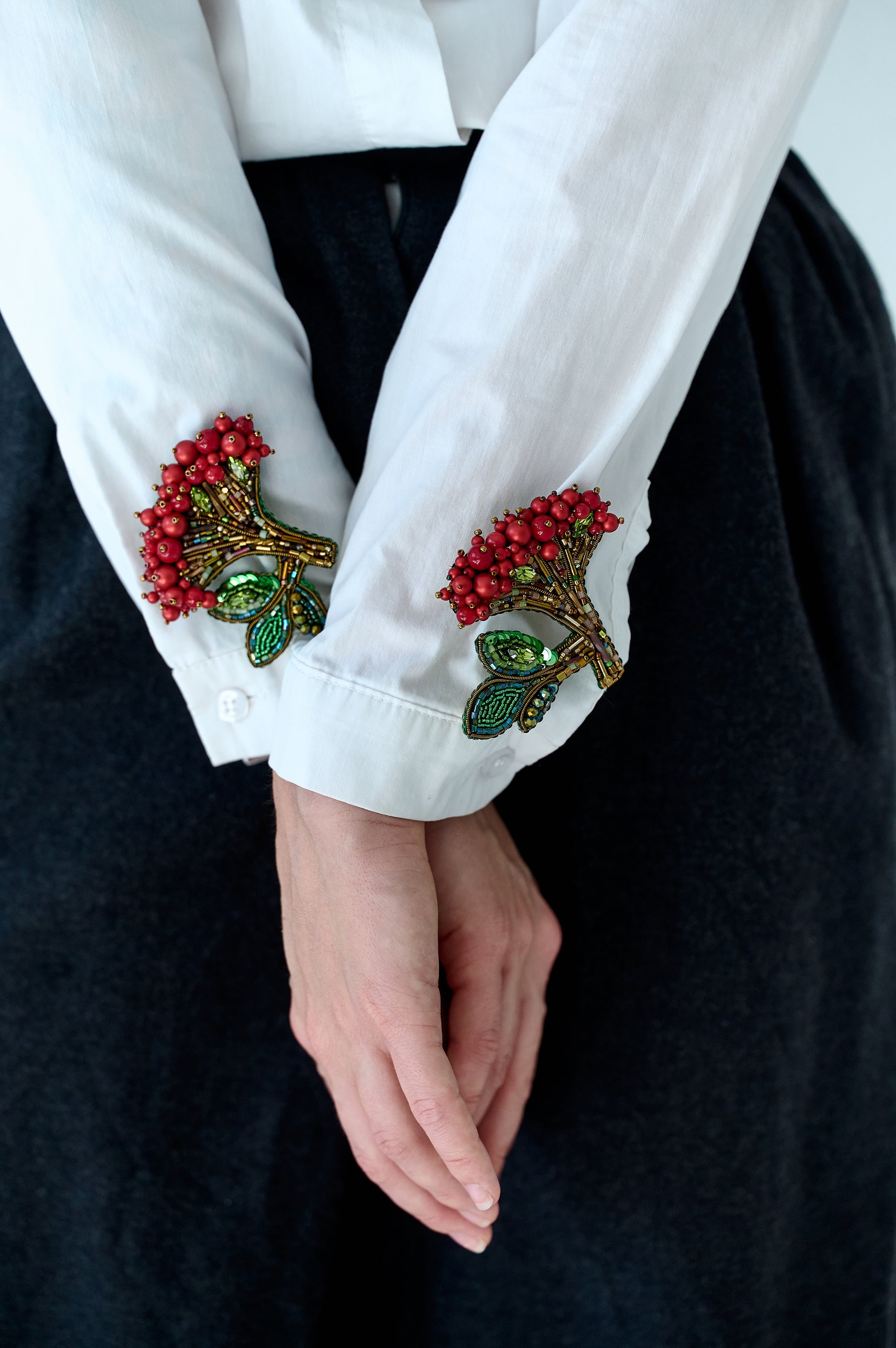 Close-up of a white shirt with decorative cuffs featuring red berries and green leaves on a black background.