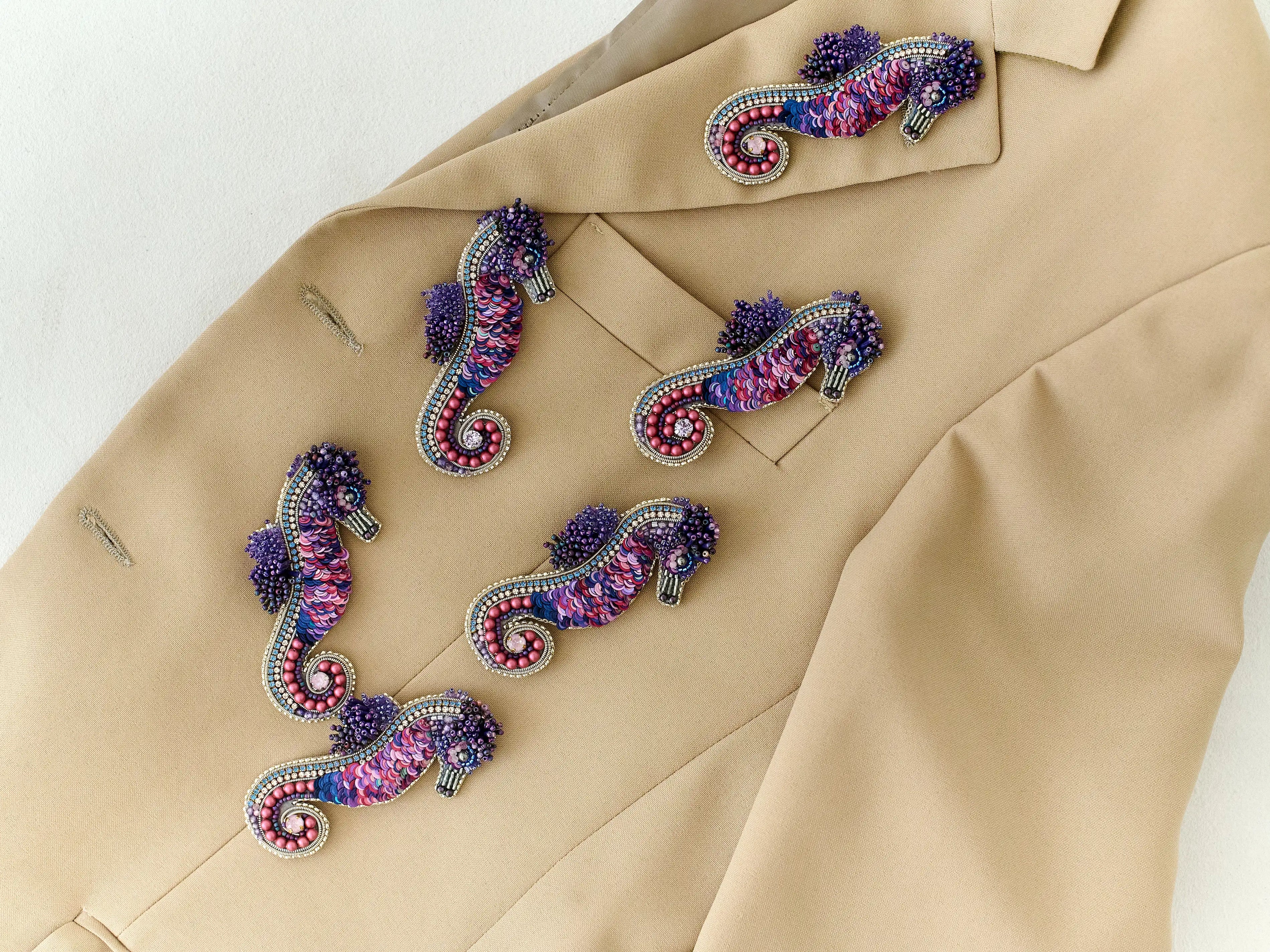 Colorful seahorse-shaped brooches on a beige jacket