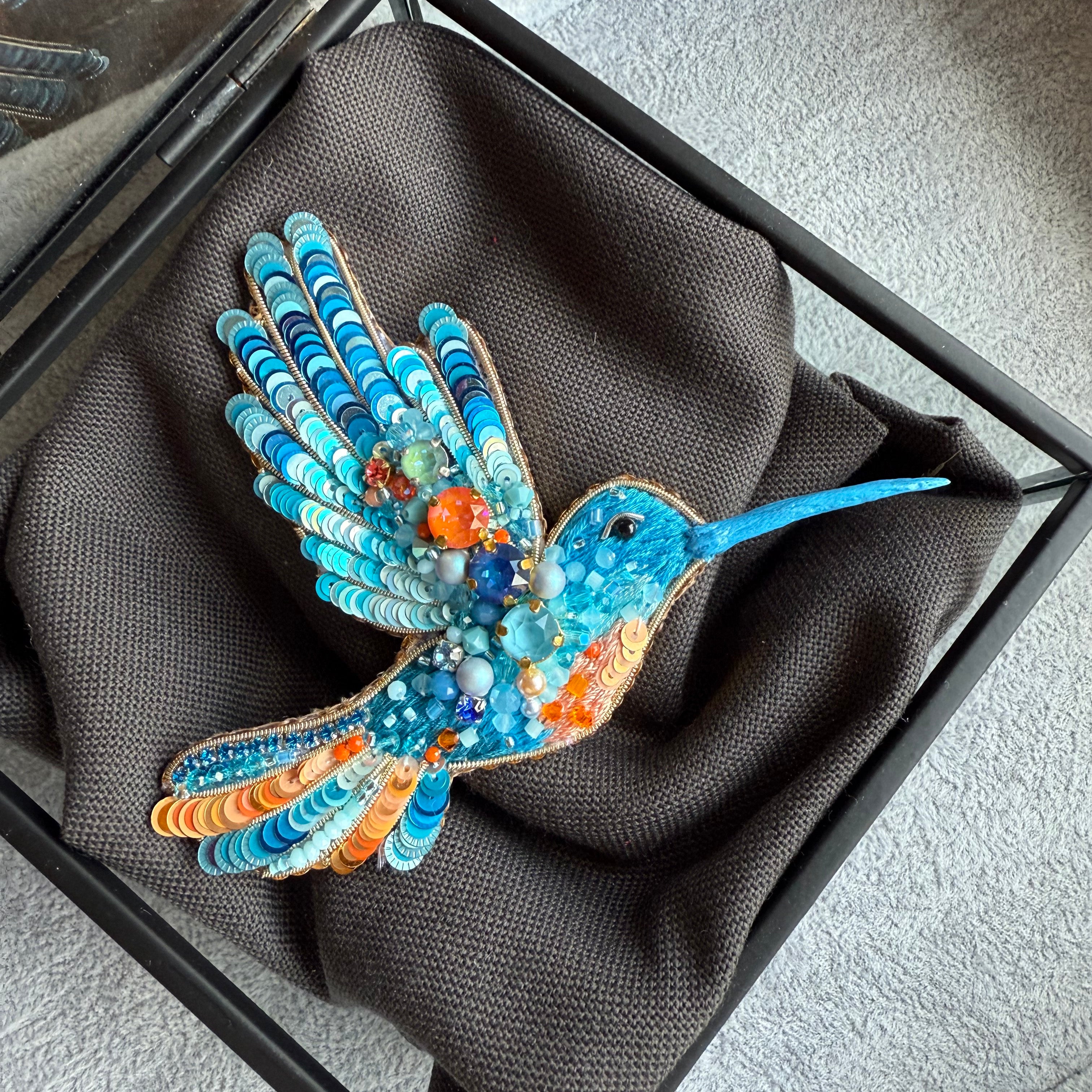 Colorful hummingbird brooch in a black box on a gray surface