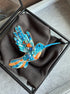 Colorful hummingbird brooch in a black box on a gray surface