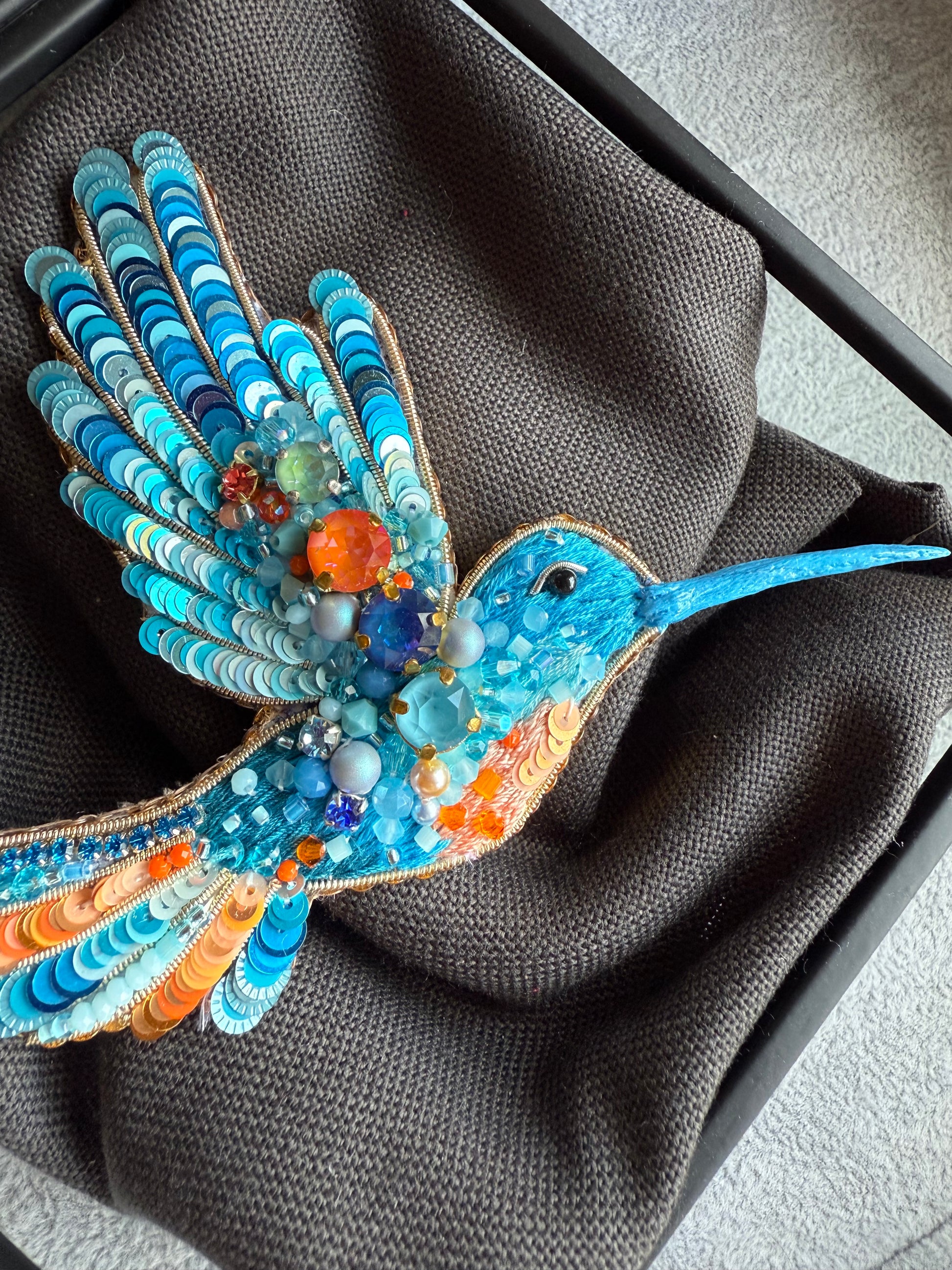 Colorful beaded hummingbird on a dark fabric background