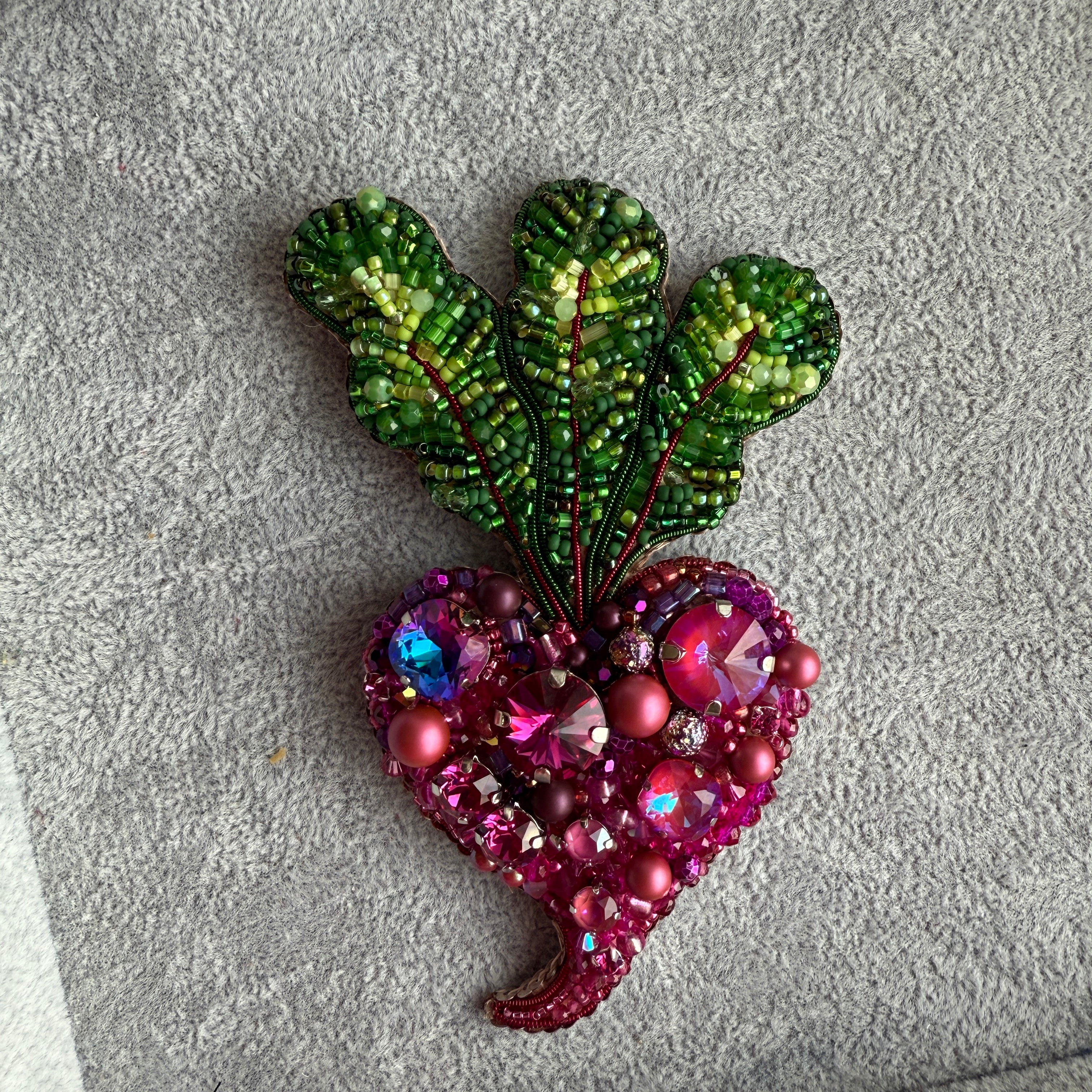 Decorative brooch with green leaf-like design and pink gemstone details on a textured surface.