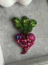 Decorative brooch with green leaf-like design and pink gemstone details on a textured surface.