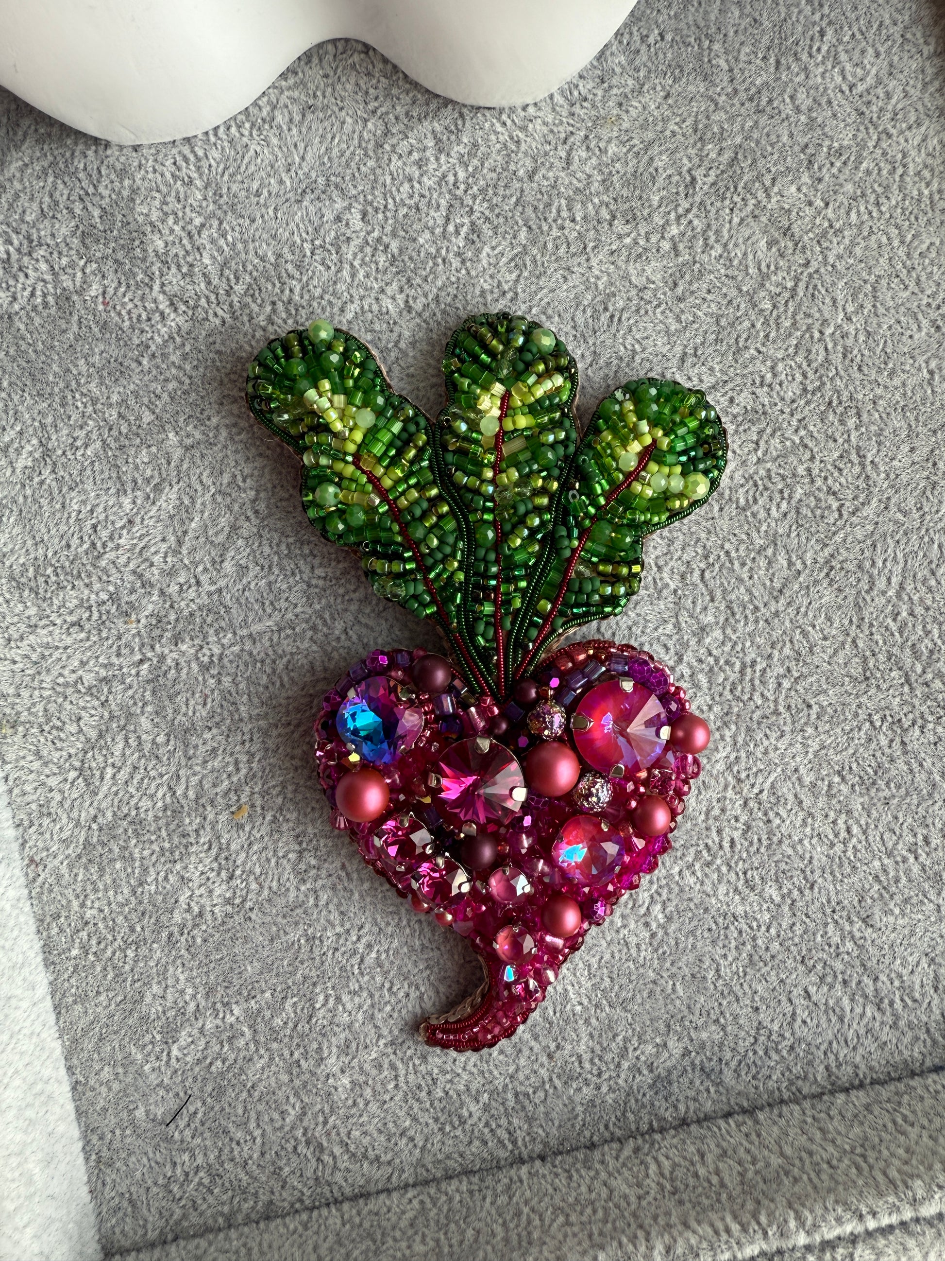 Decorative brooch with green leaf-like design and pink gemstone details on a textured surface.