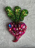 Decorative brooch with green leaf and pink gemstone on a textured gray background