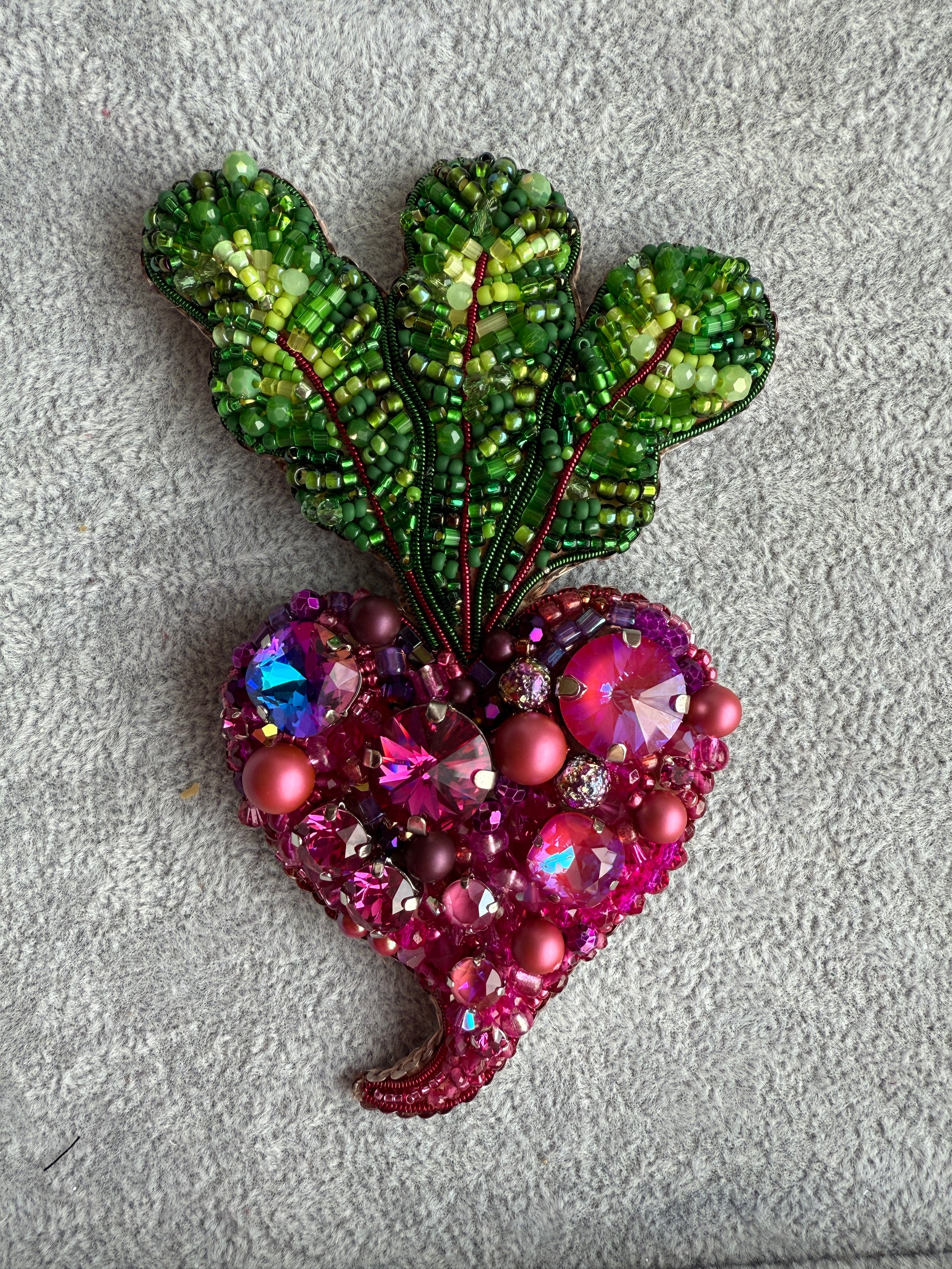 Decorative brooch with green leaf and pink gemstone on a textured gray background