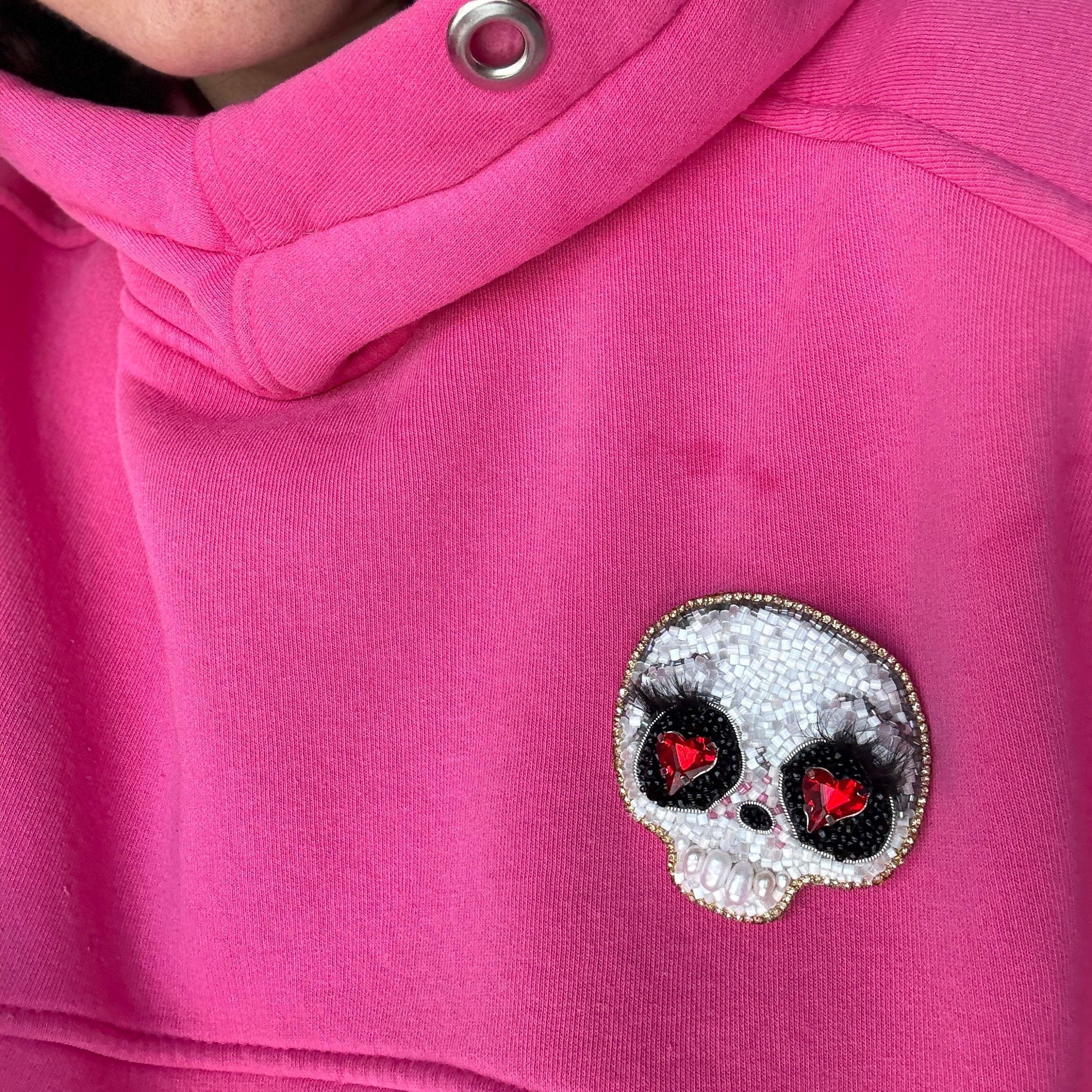 Close-up of a pink hoodie with a decorative skull patch on the chest.