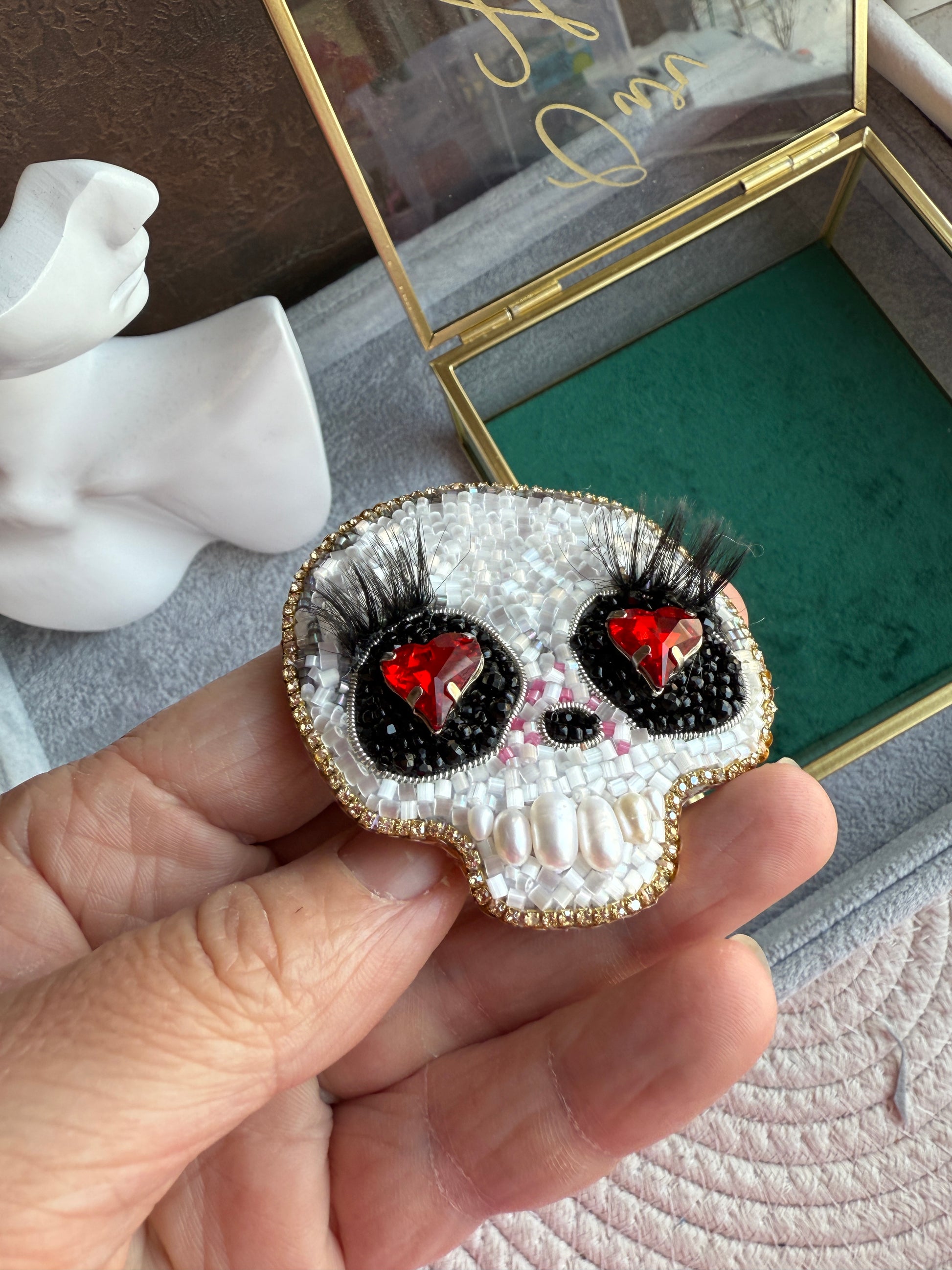 Hand holding a decorative brooch with red gemstones and black accents, set against a blurred background.