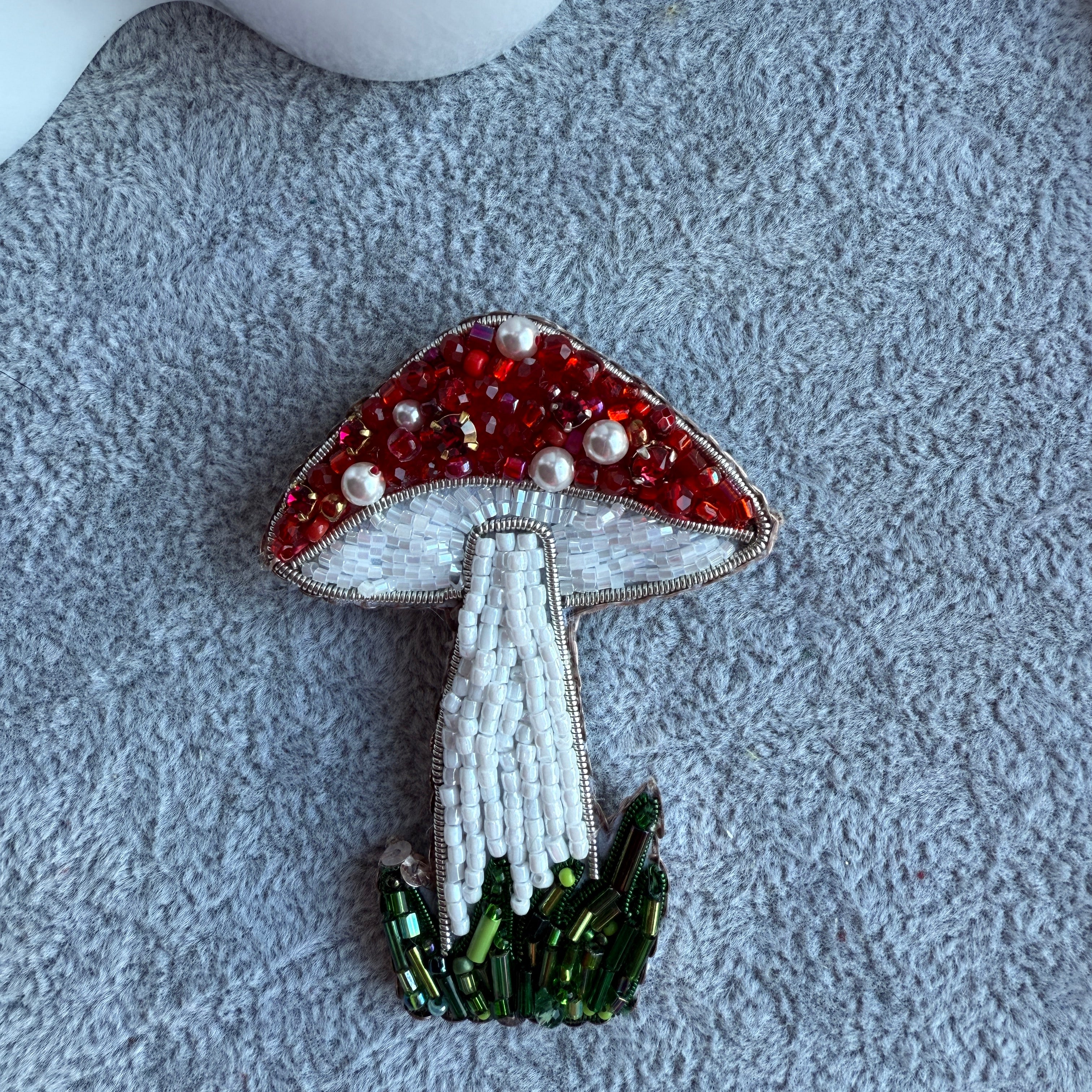 Decorative mushroom brooch with red, white, and green beads on a textured surface