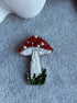 Decorative mushroom brooch with red, white, and green beads on a textured surface