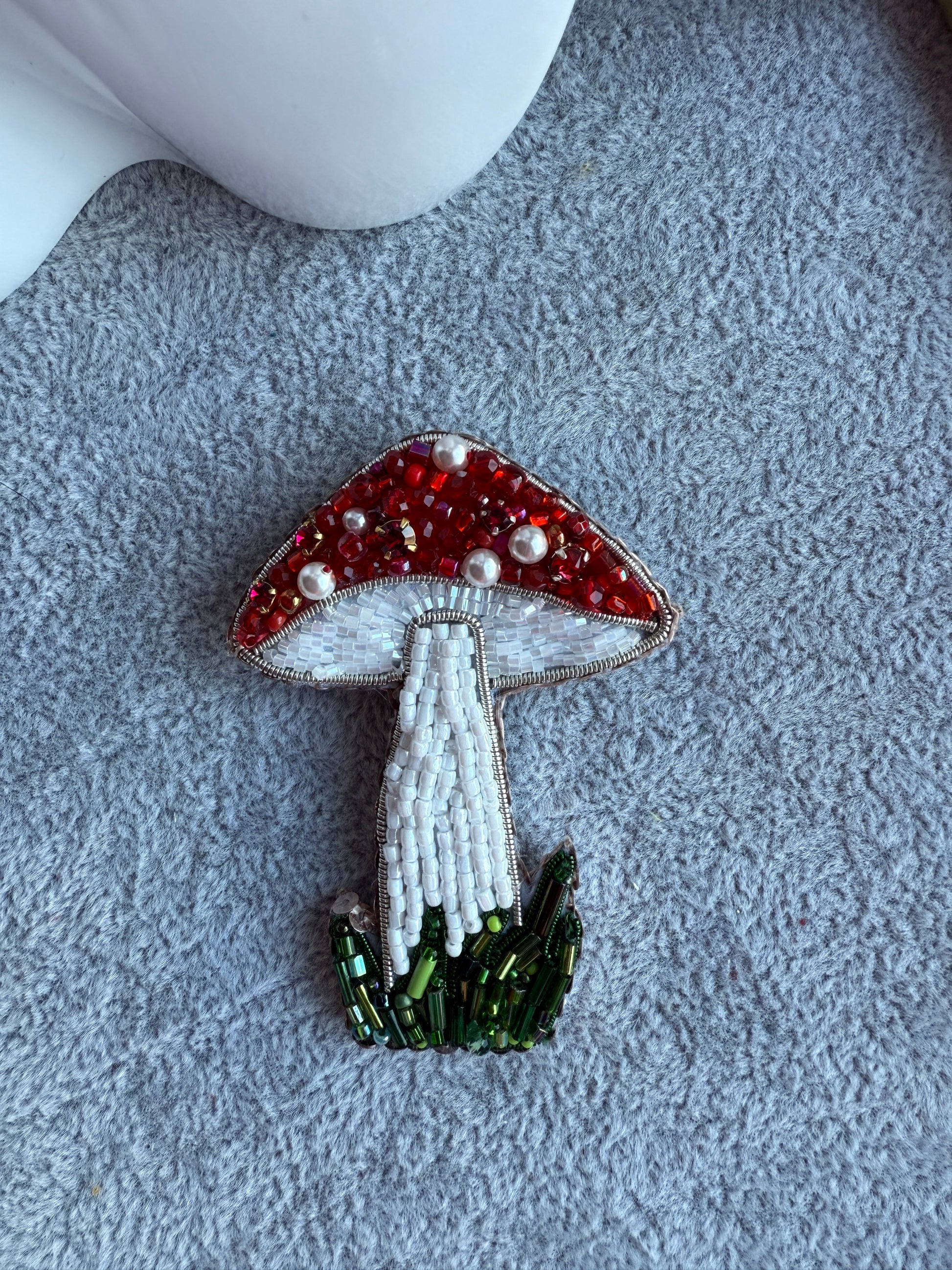 Decorative mushroom brooch with red, white, and green beads on a textured surface