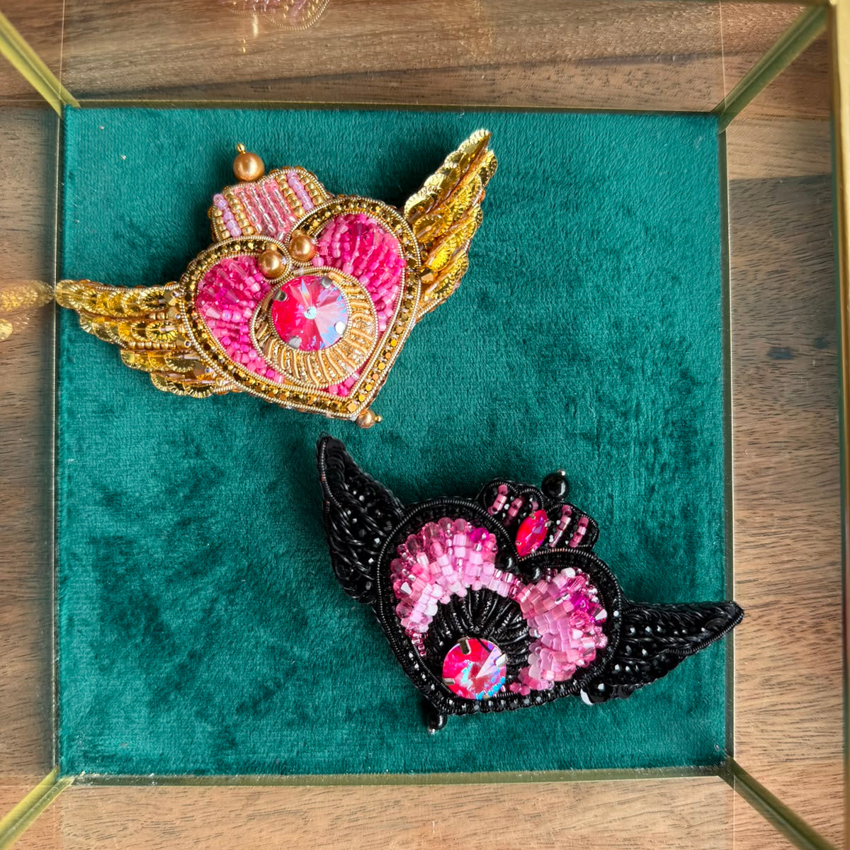Two handmade Sailor Moon inspired heart brooches in black and pink and gold and pink color options, decorated with sparkling crystals.