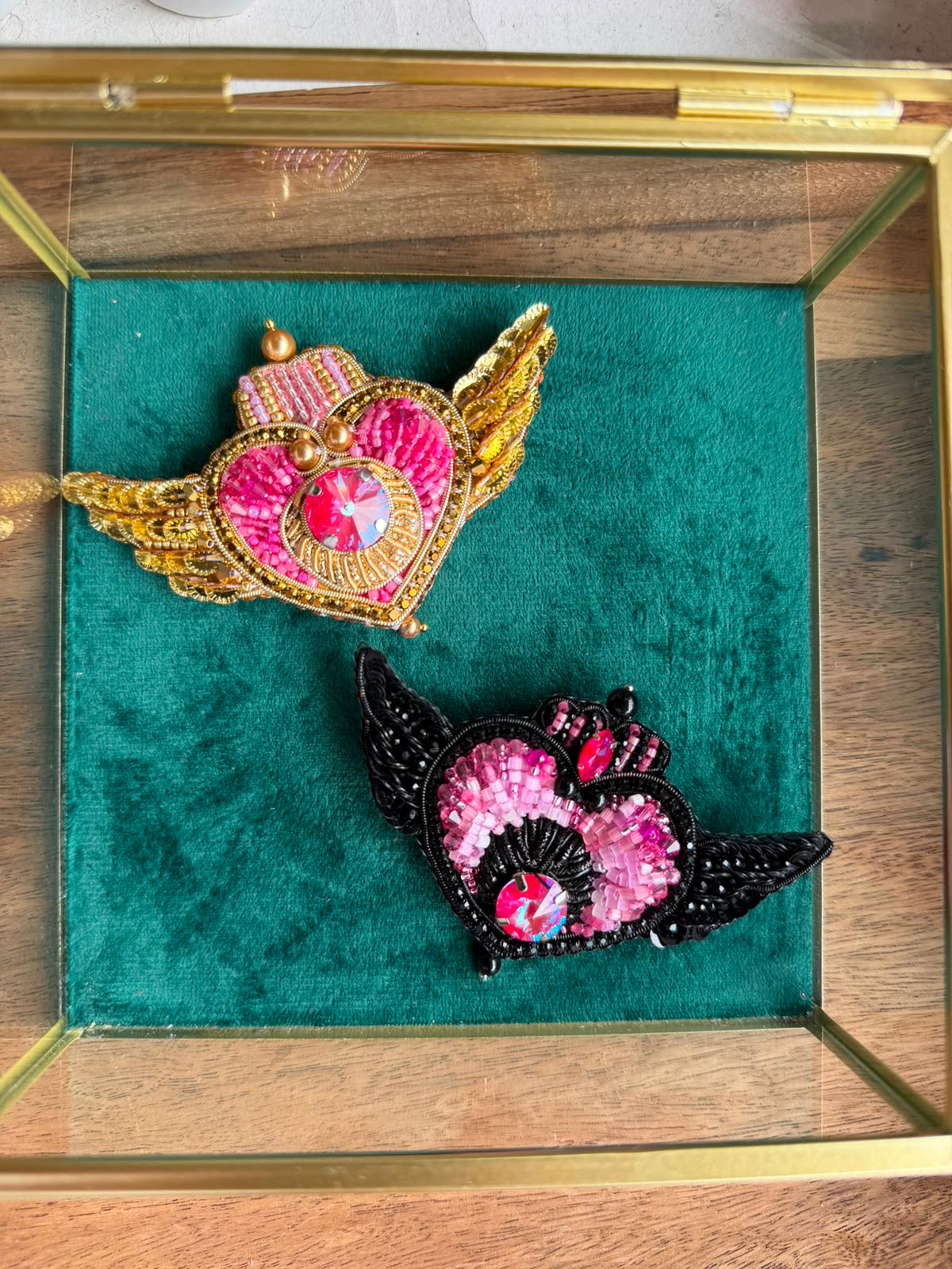 Two handmade Sailor Moon inspired heart brooches in black and pink and gold and pink color options, decorated with sparkling crystals.