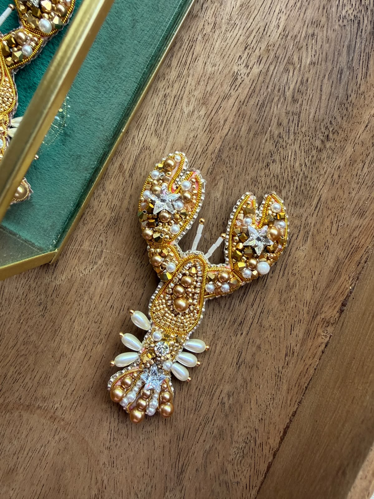 Close-up of a golden lobster accessory embroidered with glass beads, shimmering crystals, pearl accents, and intricate gold details.
