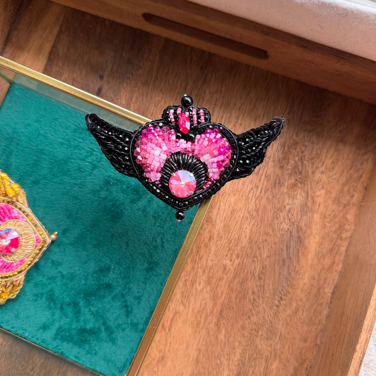 Handmade Sailor Moon inspired black winged heart brooch with pink crystal embroidery and red gemstone accent, displayed in hand.