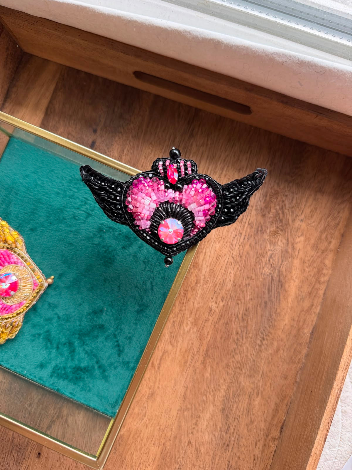 Handmade Sailor Moon inspired black winged heart brooch with pink crystal embroidery and red gemstone accent, displayed in hand.