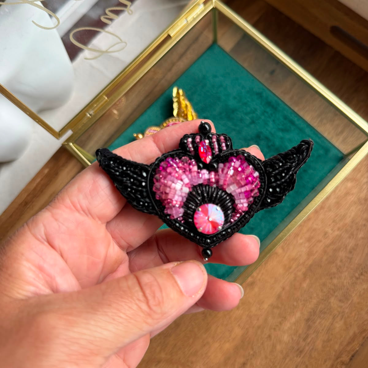Close-up of black Sailor Moon inspired heart brooch with intricate black beadwork, sparkling pink crystals, and decorative wings.