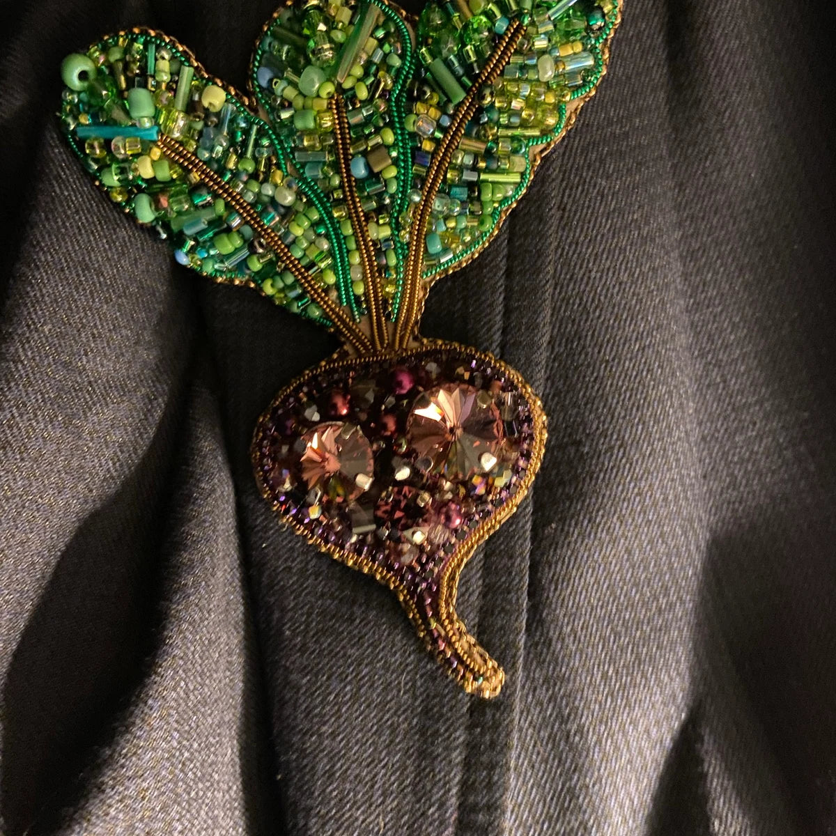 Decorative brooch with green leaf design on a gray fabric background