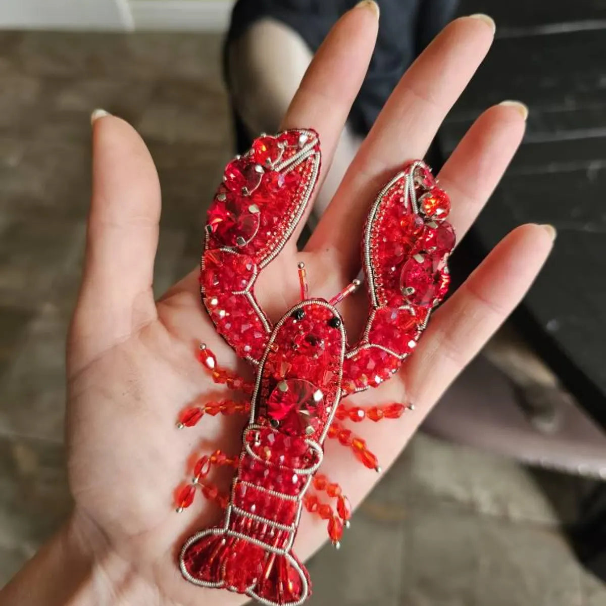Hand holding a red beaded lobster ornament against a blurred background